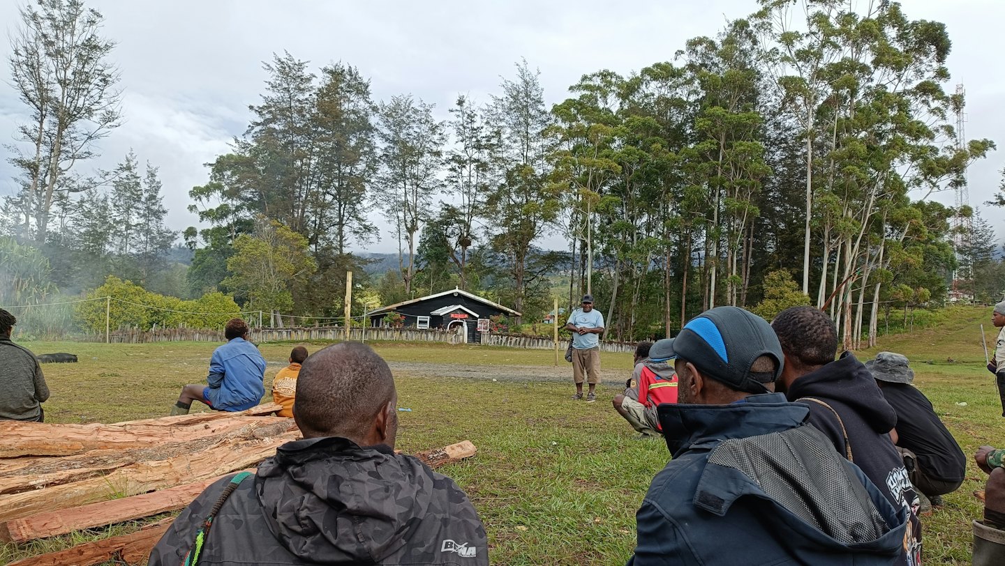 Un grupo de hombres se reúne en un campo para escuchar a un orador.